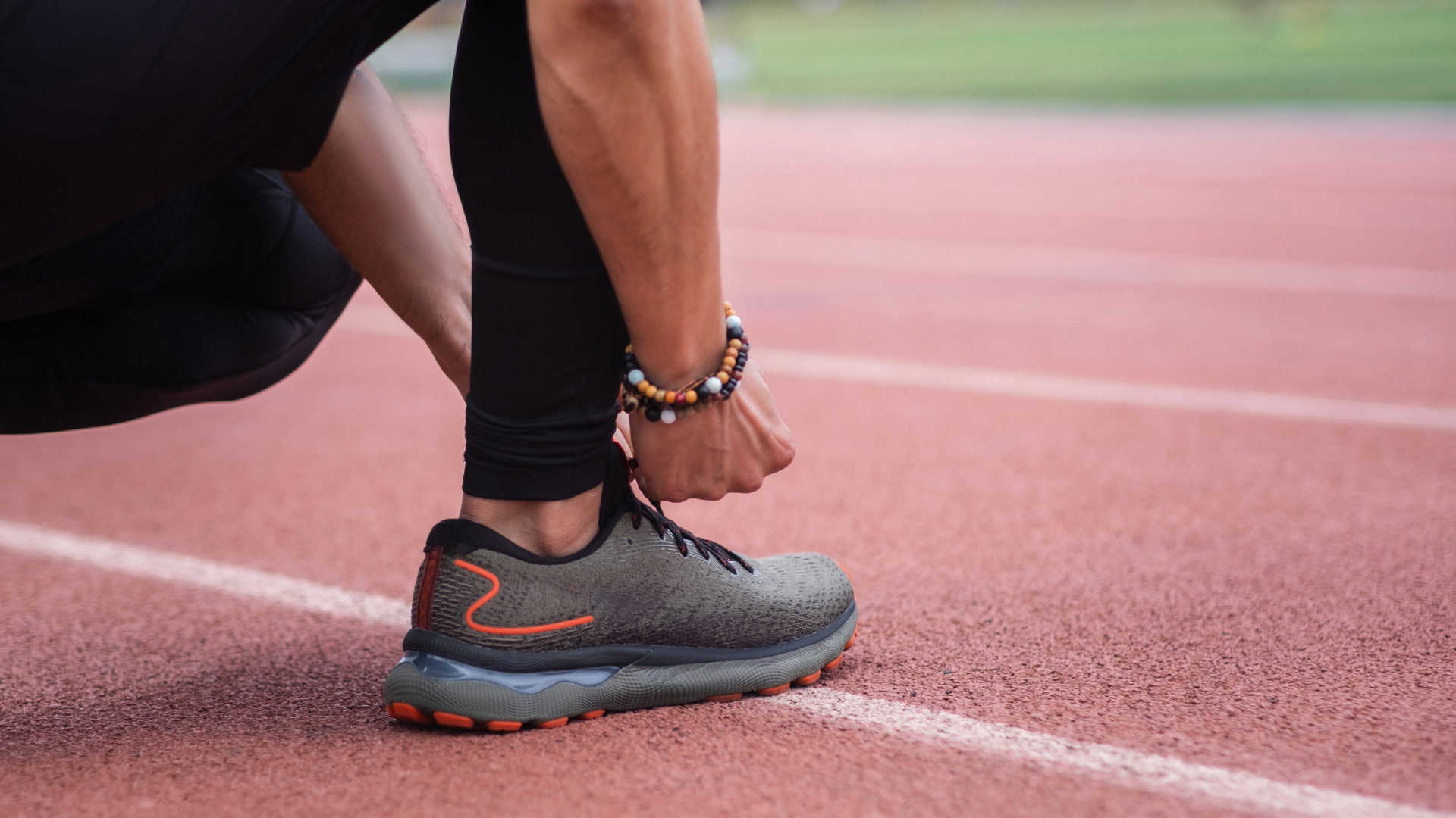 Piso Emborrachado Monolítico de Pneu Reciclado, Aplicado em uma pista de corrida. Na imagem um homem agachado amarra seu tênis para iniciar a prática esportiva, ao fundo o destaque do piso de borracha da pisoleve.